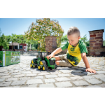 Un niño con una camiseta de John Deere juega con un modelo de tractor de orugas John Deere 9620RX verde y amarillo.