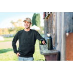 Un hombre con una sudadera negra de John Deere y una gorra beige, sosteniendo una taza negra de John Deere junto a una botella de agua en una repisa de madera.