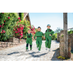 Três crianças a usar roupa de trabalho John Deere verde, incluindo fatos-macaco e macacões com detalhes em preto e amarelo, a andar em frente.