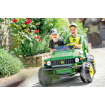 Front-side view of two smiling children in a green John Deere ride-on utility vehicle with yellow wheels and a front bumper.