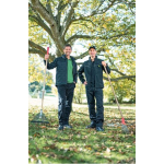 Deux hommes vêtus de vestes et de pantalons de travail John Deere sombres sourient à l’extérieur, tenant des râteaux parmi les feuilles mortes.