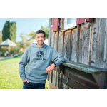Un homme souriant porte un sweat à capuche gris John Deere avec une poche avant, debout à l’extérieur.