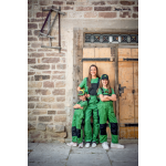 Een vrouw en twee meisjes staan lachend in groene John Deere-werkoveralls met zwarte kniestukken en merkmutsen.