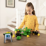 A young girl plays with a green John Deere build-it-yourself tractor toy, disassembled on a wooden table.