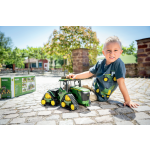 Vista frontal lateral de un modelo de tractor de orugas John Deere 9620RX verde y amarillo con el que un niño está jugando.