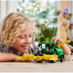 A child smiles while looking at a green and yellow LEGO Technic John Deere 9620R 4WD Tractor model with a front attachment.