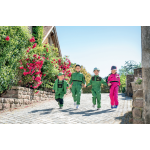 Vier kinderen, drie in groene en één in roze John Deere-overalls, lopen hand in hand over een geplaveid pad.
