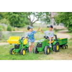 Deux garçons portant des chemises et des casquettes John Deere se tapent dans la main, l’un sur un petit tracteur vert avec remorque, l’autre à côté d’un petit chargeur.